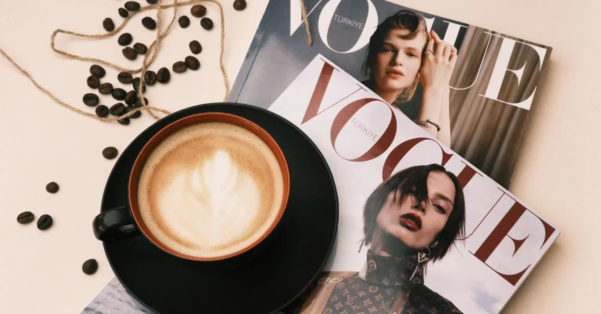 Une table de café confortable avec un café au lait et des magazines Vogue, parfaite pour une détente élégante.