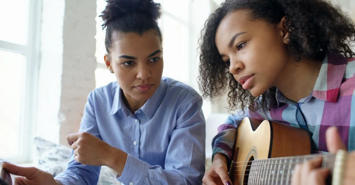 Femme enseignant à sa fille à jouer de la guitare à l'intérieur par une journée ensoleillée.