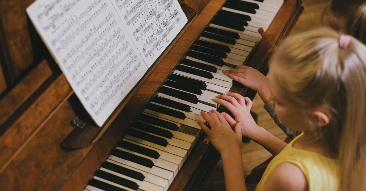 Une jeune fille aux cheveux blonds jouant du piano, suivant des partitions à l'intérieur.