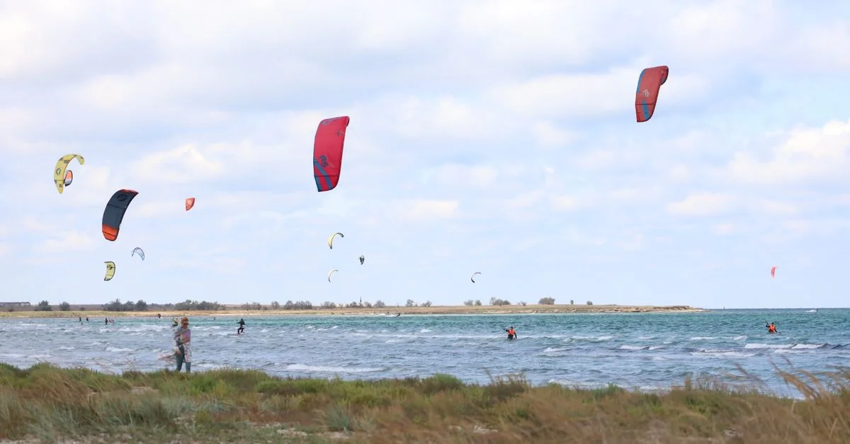 Des kitesurfeurs passionnés chevauchent les vagues sous un ciel nuageux dynamique au bord de l'océan.
