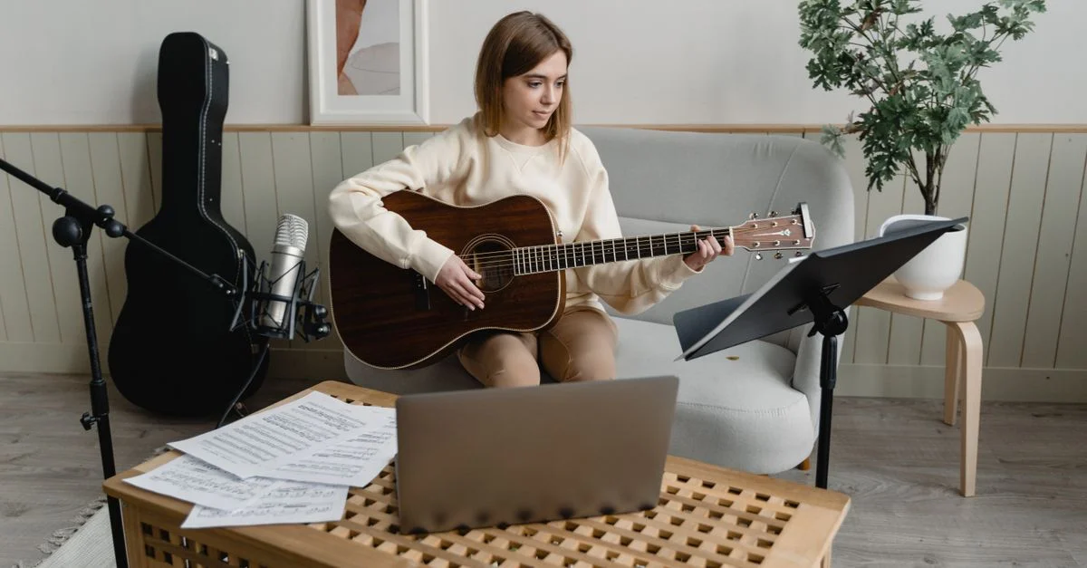 Femme pratiquant la guitare à l'intérieur avec des partitions et un microphone. Idéal pour des thèmes liés aux loisirs musicaux.